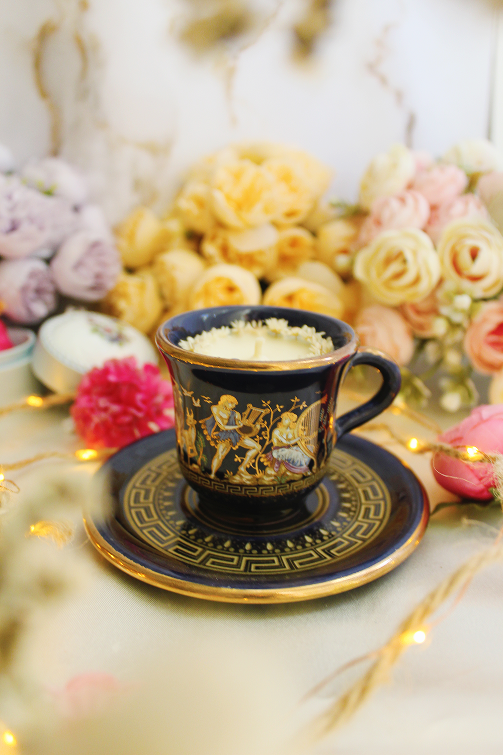 Gros plan d’une bougie dans une tasse bleu profond ornée de motifs grecs dorés.